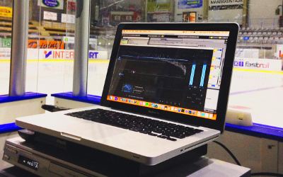 The Skating Music Guy's laptop at rinkside in an ice arena, with mastering software open on the screen